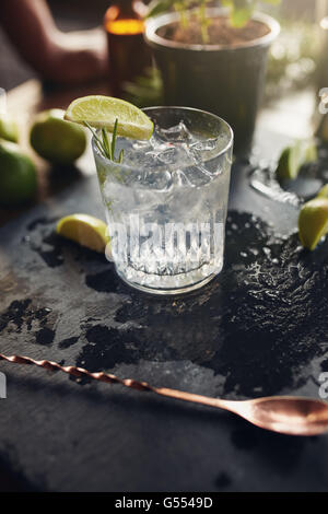 Glass of fresh cocktail drink with lemon slice and ice cubes on a black board. Stock Photo