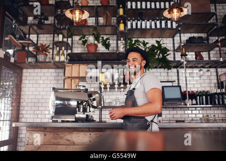 Indoor shot of happy young bar owner standing at the counter and looking away smiling