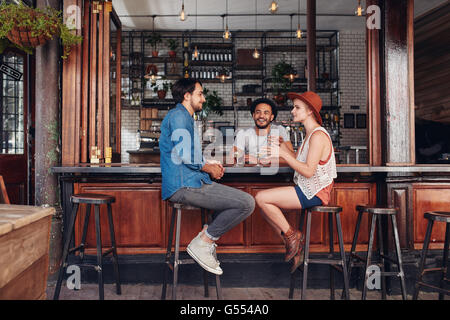 Portrait of happy group of young people meeting in a coffee shop and talking. Three young friends sitting at a cafe table. Stock Photo