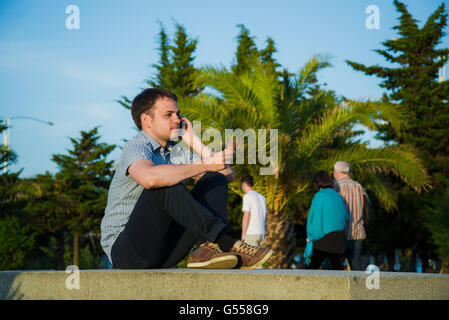 Young man at promenade eating an ice-cream and using his phone, maybe he is single or waiting for someone Stock Photo