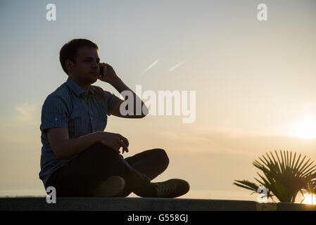 Man on phone sits on bench near the sea beach Stock Photo