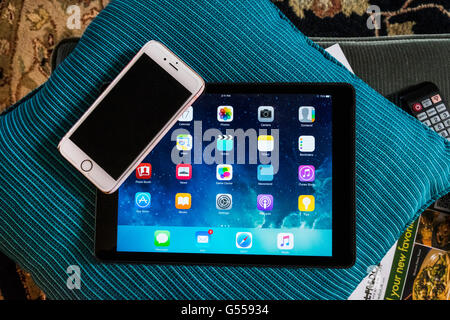 An iPhone 6s lying on an iPad Air showing the start screen while lying on a sofa cushion in a messy environment indoors. USA. Stock Photo