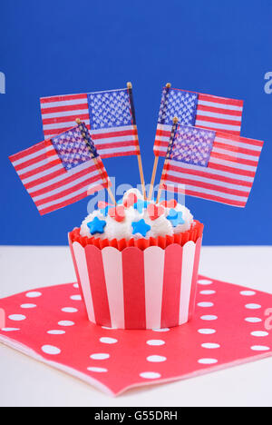 USA theme cupcake with red hearts and blue star candy decorations and American flags on a red, white and blue background. Stock Photo