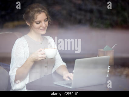 Portrait of young happy beautiful female in coffee shop. Woman sitting in modern urban cafe and working on laptop