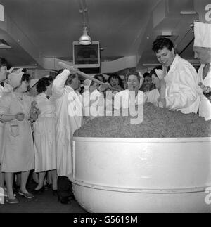 With the aid of a long wooden stirring spoon comedian Charlie Drake, left, tempts one of the women workers at Cadby Hall, London, with part of the mix of a giant 160 pound Christmas pudding. Digging his spoon in the ingredients is pop singer Cliff Richard. The ingredients for the pudding are a gift of the dried fruit growers of Australia to the old people of the City of London. Stock Photo