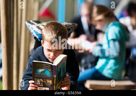 A young boy reading a paperback book by Bear Grylls at  the annual The Hay Festival of Literature and the Arts, 'the Woodstock of the Mind', Hay on Wye, Powys, Wales  UK May-June 2016 Stock Photo