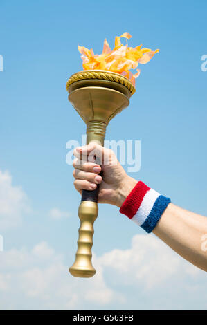 Hand of an American torchbearer athlete wearing USA red, white, and blue colors sweatband holding sport torch in the sky Stock Photo