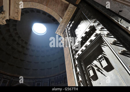 Pantheon Rome with strong shafts of sunlight coming through the ceiling light racking across the studs on the door Stock Photo