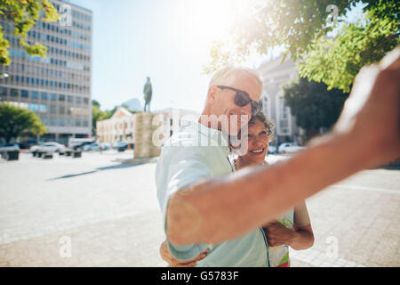 Happy and affectionate senior couple embracing and taking a selfie outdoors. Tourist taking self portraits on their summer vacat Stock Photo