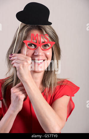 Half Body Shot of a Happy Middle Aged Woman Holding Funny Photo Booth Props and Smiling at the Camera Against Gray Brown Wall. Stock Photo