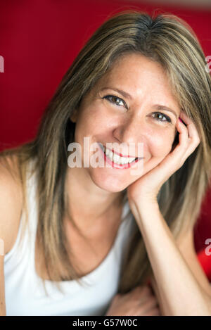 Close up Attractive Adult Woman Leaning her Face on her Hand and Smiling at the Camera Against Red Background. Stock Photo