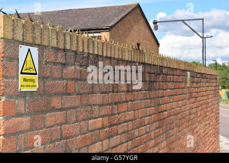 Brick Wall with security climb spikes and warning sign Stock Photo