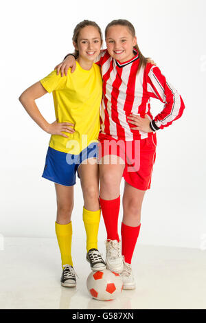 Team captains of girls football match posing with a ball against a white background. They both have one foot on the ball and one Stock Photo