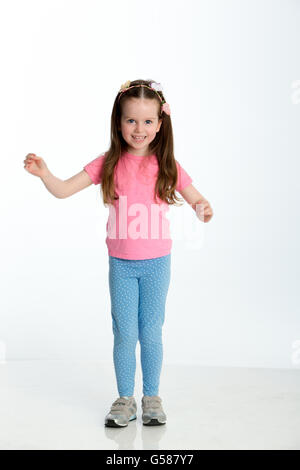 Young girl posing for the camera with her arms out. She is standing against a white background and is smiling at the camera. Stock Photo