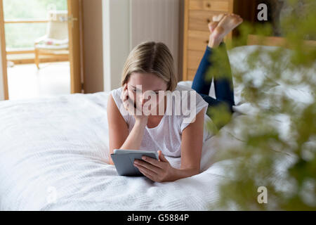 Woman lying on her bed at home using a digital tablet Stock Photo