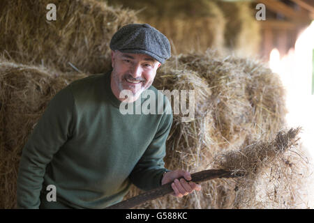 Happy man smiling for the camera as he mucks out a stable Stock Photo