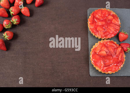 Chocolate tart, tartalette with white chocolate and mascarpone cream, fresh strawberries on top. Border of whole fresh ripe red Stock Photo