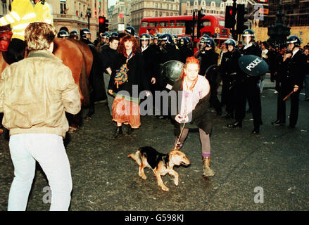 A woman leads her dog away from a line of policemen in riot gear after a protest against the so-called Poll Tax erupted into a riot affecting Trafalgar Square and the surrounding area of central London. Stock Photo