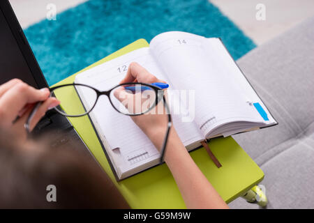 View through glasses to the open blank page of a business journal or diary with a woman's hand, who holding a pen for making appointments, organising a schedule or agenda. Stock Photo