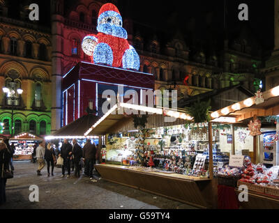 People shopping on Christmas market and town hall with Big Santa on Albert Square at night, Manchester, England, UK
