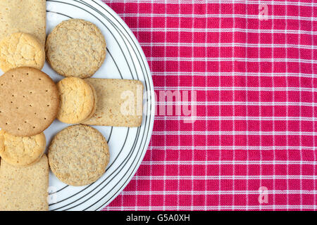 Assorted biscuits arranged on a white pattened plate on a red and white rustic napkin Stock Photo
