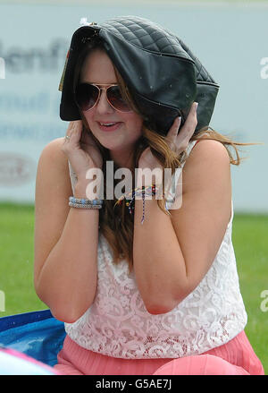 Horse Racing - 2012 John Smiths Northumberland Plate Day - Newcastle Racecourse. A racegoer uses her bag as shelter from a rain shower during the 2012 John Smiths Northumberland Plate Day at Newcastle Racecourse. Stock Photo