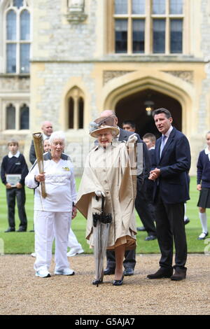 Queen Elizabeth II and the Duke of Edinburgh (centre obscured) with LOCOG chairman Lord Sebastian Coe (right) with Torchbearer 073 Gina Macgregor as she holds the Olympic Flame outside Windsor Castle, Berkshire. PRESS ASSOCIATION Photo. Picture date: Tuesday July 10, 2012. See PA story OLYMPICS Torch. Photo credit should read: Steve Parsons/PA Wire Stock Photo