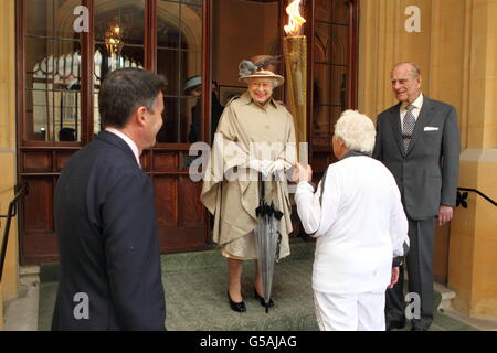 Queen Elizabeth II looks at the Olympic Flame held by Torchbearer 073 Gina Macgregor as LOCOG chairman Lord Sebastian Coe (left) and the Duke of Edinburgh (right) look on at Windsor Castle, Berkshire. PRESS ASSOCIATION Photo. Picture date: Tuesday July 10, 2012. See PA story OLYMPICS Torch. Photo credit should read: Steve Parsons/PA Wire Stock Photo