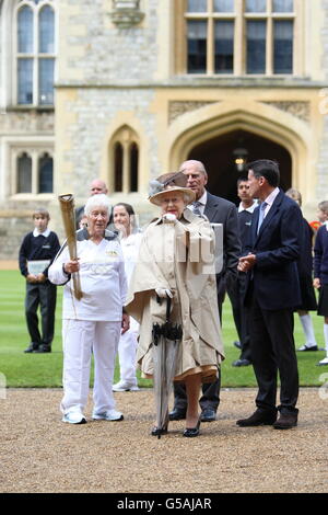 Queen Elizabeth II and the Duke of Edinburgh (centre right partially obscured) with LOCOG chairman Lord Sebastian Coe (right) with Torchbearer 073 Gina Macgregor as she holds the Olympic Flame outside Windsor Castle, Berkshire. PRESS ASSOCIATION Photo. Picture date: Tuesday July 10, 2012. See PA story OLYMPICS Torch. Photo credit should read: Steve Parsons/PA Wire Stock Photo