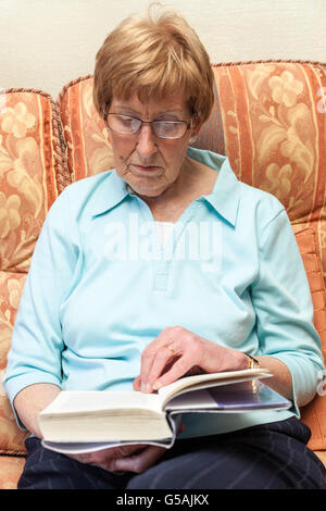 Older person with glasses reading a book at home Stock Photo