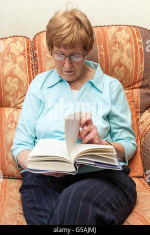 Senior woman turning a page of a book that she is reading at home Stock Photo