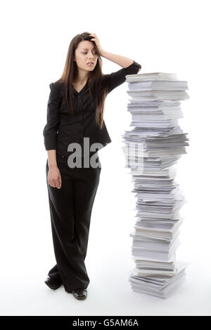 business woman standing against a large pile of paper work not looking very happy Stock Photo