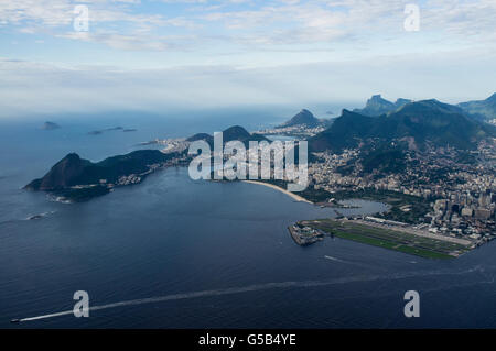 Aerial view of part of Rio de Janeiro south zone & mountains and Santos Dumont Airport ( right ), at the border of Guanabara Bay, the second major airport serving the city - it is named after the Brazilian aviation pioneer Alberto Santos Dumont (1873–1932) - Sugar Loaf mountain at left, Corcovado with its Christ the Redeemer statue at center / right surrounded by Tijuca Forest and Pedra da Gavea in background. Stock Photo