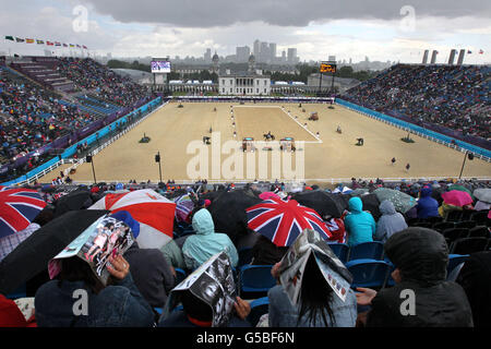 Crowds shelter under umbrellas and newspapers during a heavy rain shower as they watch Great Britain's Kristina Cook on Miners Frolic compete during the Dressage stage of the Eventing at Greenwich Park, London on the second day of the London 2012 Olympics. Stock Photo