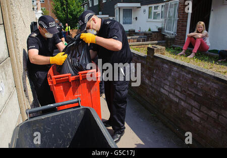 Residents watch as police officers search through rubbish bins near Tia Sharp's grandmother's home in New Addington, London. Stock Photo