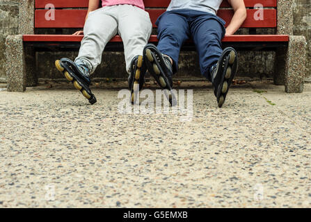 People friends in training suit with roller skates. Woman and man relaxing on bench outdoor. Stock Photo