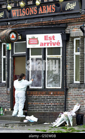 A police officer checks for fingerprints on windows at the Wilsons Arms Pub, Leeds, where a father-of-one was gunned down while children played party games. Former professional Rugby League star David Nelson, 38, was shot in the head at the pub in Seacroft on 22/07/01. *...Floral tributes to Mr Nelson are piled on the right. Stock Photo