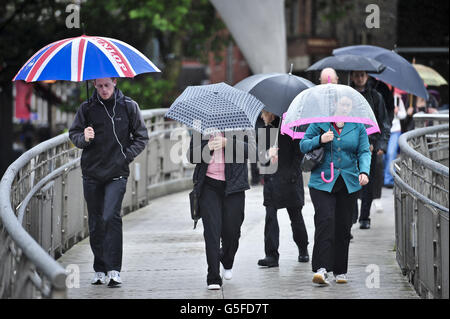 Commuters with umbrellas make their way across Millennium Bridge in Bristol, where there has been heavy rain and a MET office weather warning issued for the South West. Stock Photo
