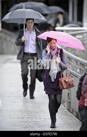 Commuters with umbrellas make their way across Millennium Bridge in Bristol, where there has been heavy rain and a MET office weather warning issued for the South West. Stock Photo