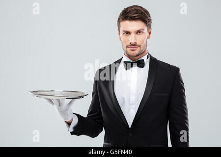 Portrait of young butler in tuxedo holding empty tray Stock Photo