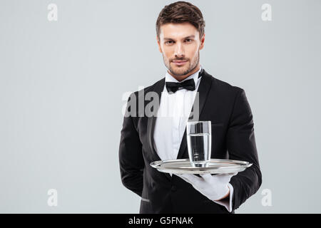 Portrait of waiter in tuxedo and gloves holding glass of water on metal tray Stock Photo