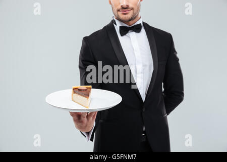 Closeup of young waiter in tuxedo holding piece of cake on plate Stock Photo