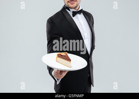 Butler in tuxedo with bowtie holding plate with piece of cake Stock Photo