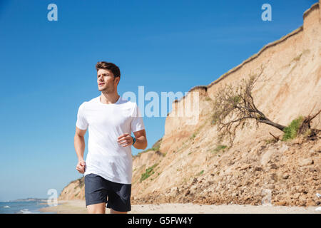 Serious young sportsman in white t-shirt and black shorts running on the beach Stock Photo