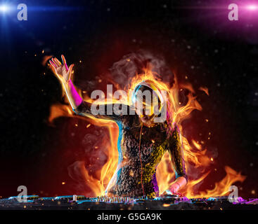 Disc jockey brunette girl mixing electronic music with fire flames around Stock Photo