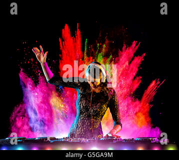Disc jockey brunette girl mixing electronic music with colored powder explosion on background Stock Photo