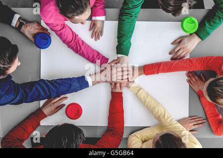 Group of people joining hands in stack sitting around the table Stock Photo