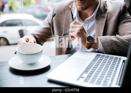 Cropped image of a businessman holding cup and using laptop in cafe indoors Stock Photo