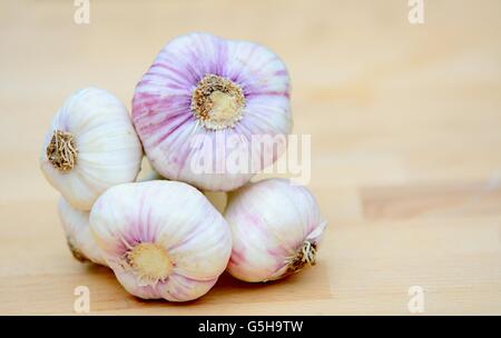 Bunch of fresh garlic with green scape on brown wood plate. Stock Photo