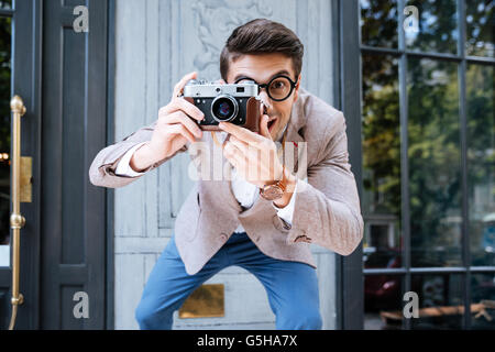 Smiling funny photographer in round glasses using old camera and taking photos outdoors Stock Photo